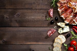 Top view of a rustic wood table with delicatessen like prosciutto, salami, black olives, crostini, blue cheese and some herbs at the right border leaving a useful copy space.  DSRL studio photo taken with Canon EOS 5D Mk II and Canon EF 100mm f/2.8L Macro IS USM